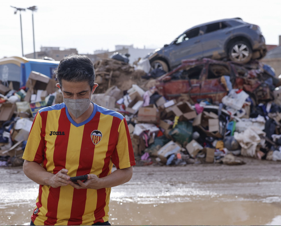 CATARROJA (VALENCIA), 08/11/2024.- Un hombre mira su teléfono junto a coches y enseres apilados en una calle de Catarroja, este viernes. Diez días después de la tragedia, los servicios de emergenci