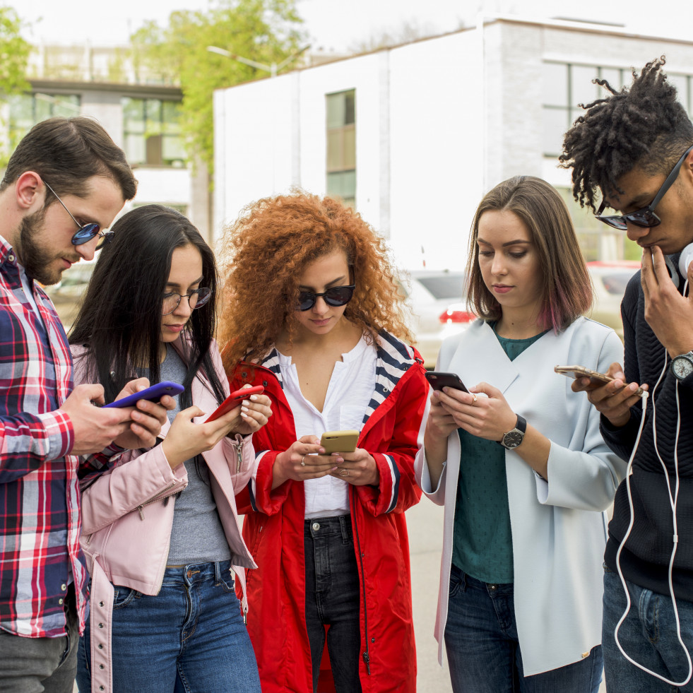 Grupo de amigos modernos usando el telefono celular al aire libre
