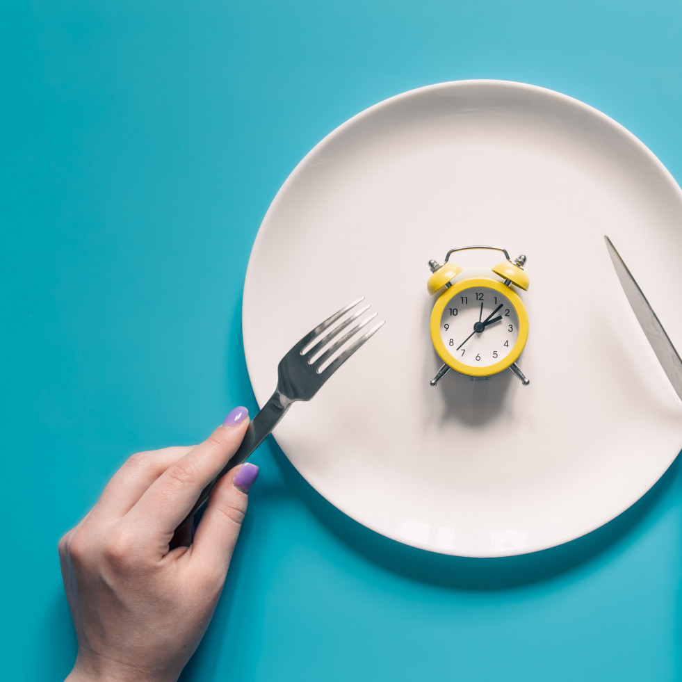 Manos sosteniendo un cuchillo y un tenedor sobre el despertador en un plato sobre fondo azul